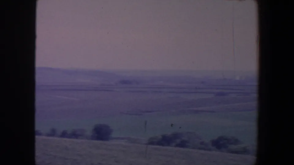 1959 Iowa rural fields and a low tree line viewed through dark window framing from a moving vehicle.