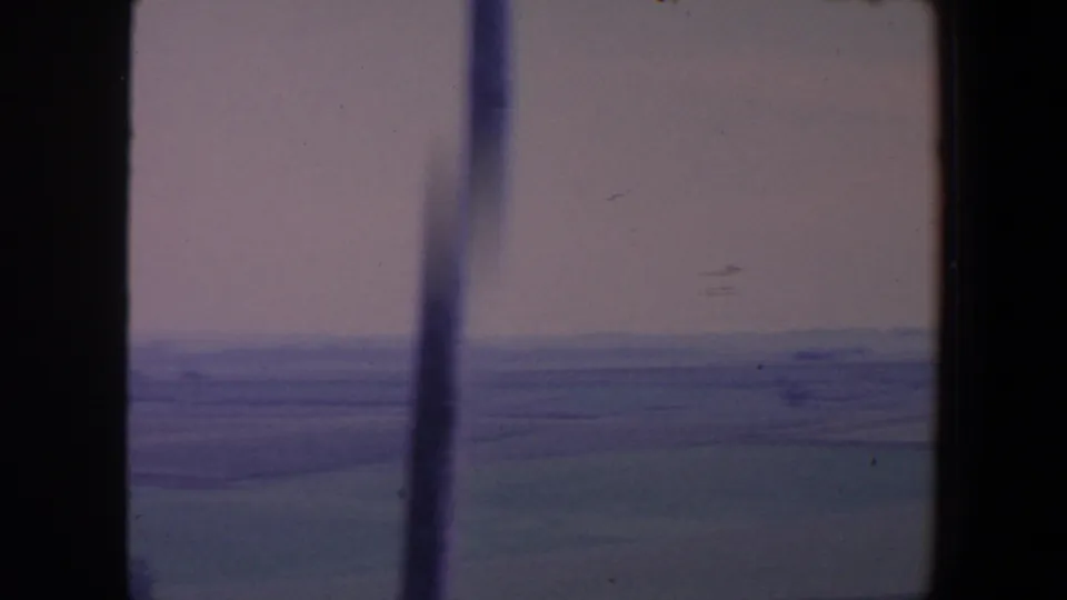 Soft 1959 Iowa countryside view with layered fields and haze, partly obscured by vertical window framing.