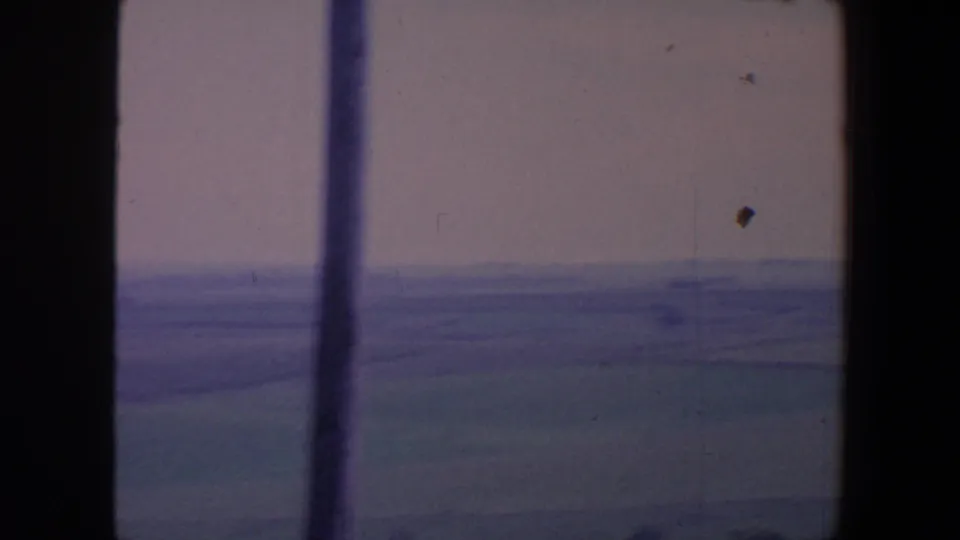 Rural Iowa fields and a faint horizon pass by in soft focus, framed by a dark window edge and film wear.