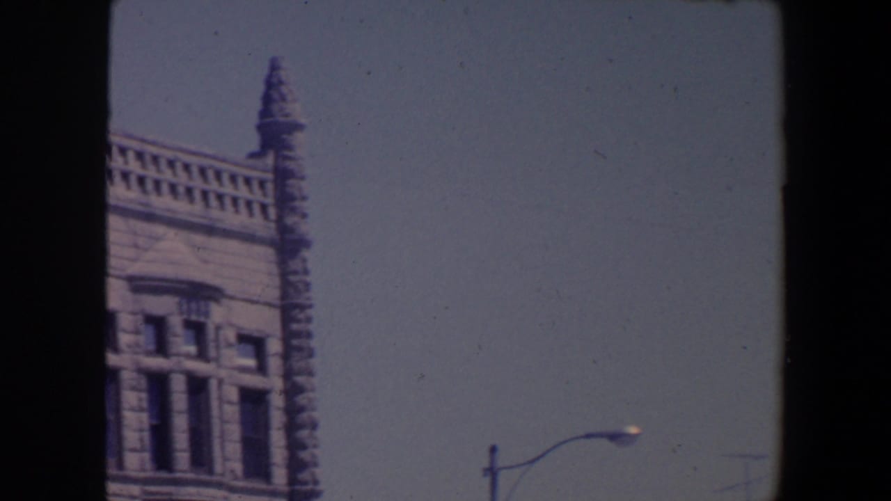 Ornate stone building corner with spire against pale blue sky.