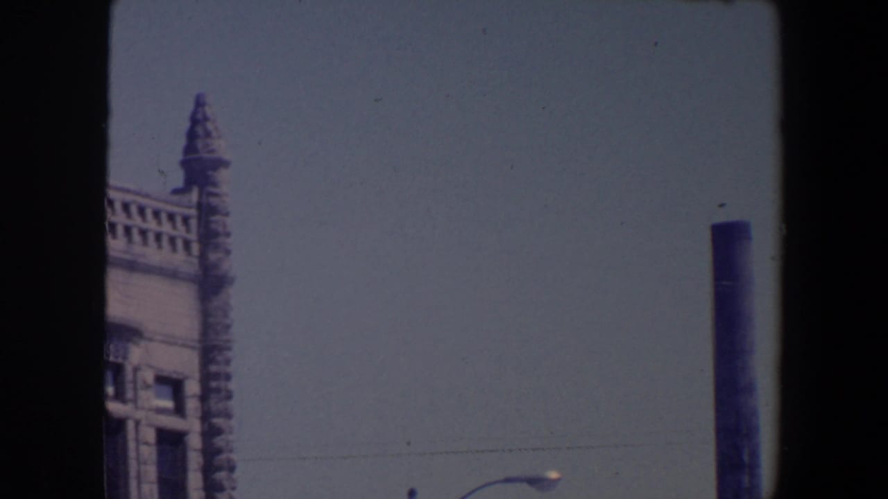 1959 Iowa street view with an ornate building edge, pale sky, streetlamp, and a dark utility pole at the right of frame.