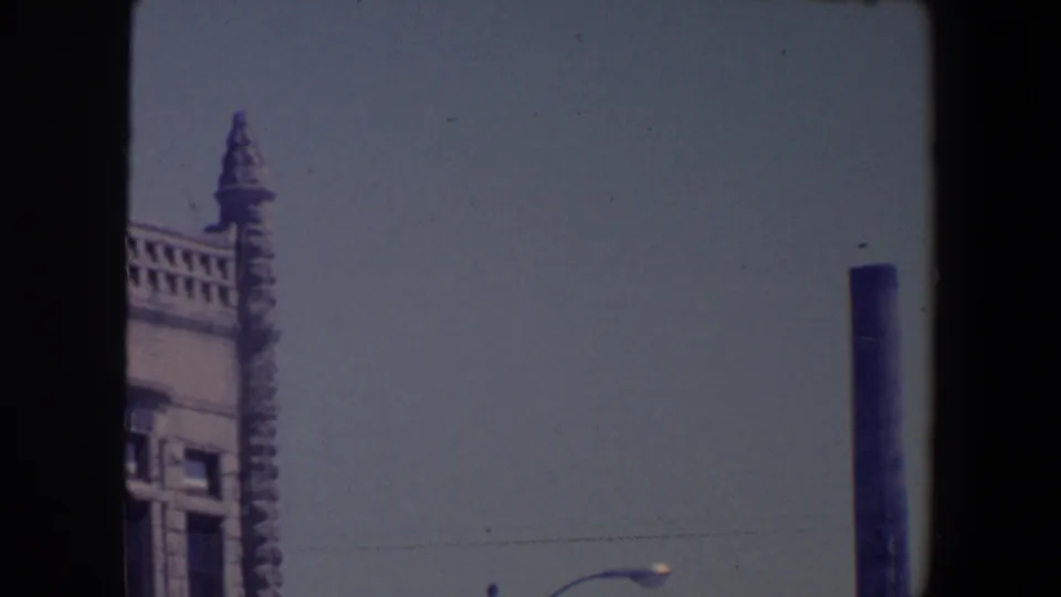 1959 Iowa street view with an ornate building edge, pale sky, streetlamp, and a dark utility pole at the right of frame.
