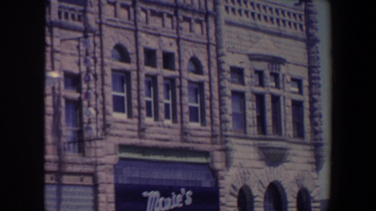 Stone commercial facade with arched windows and a dark Mae's awning.