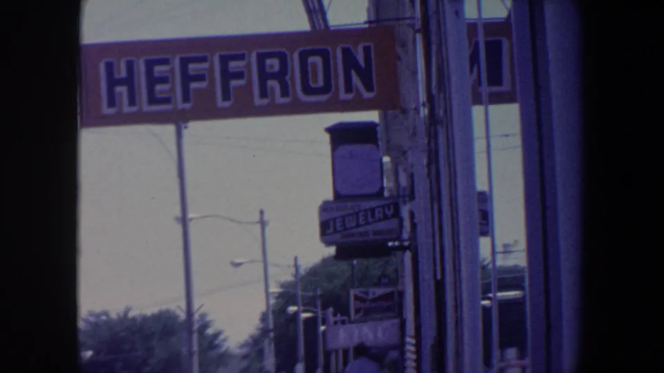 1959 Iowa frame showing the Heffron sign across a storefront, a jewelry sign below, street lamps, and nearby shopfront details.