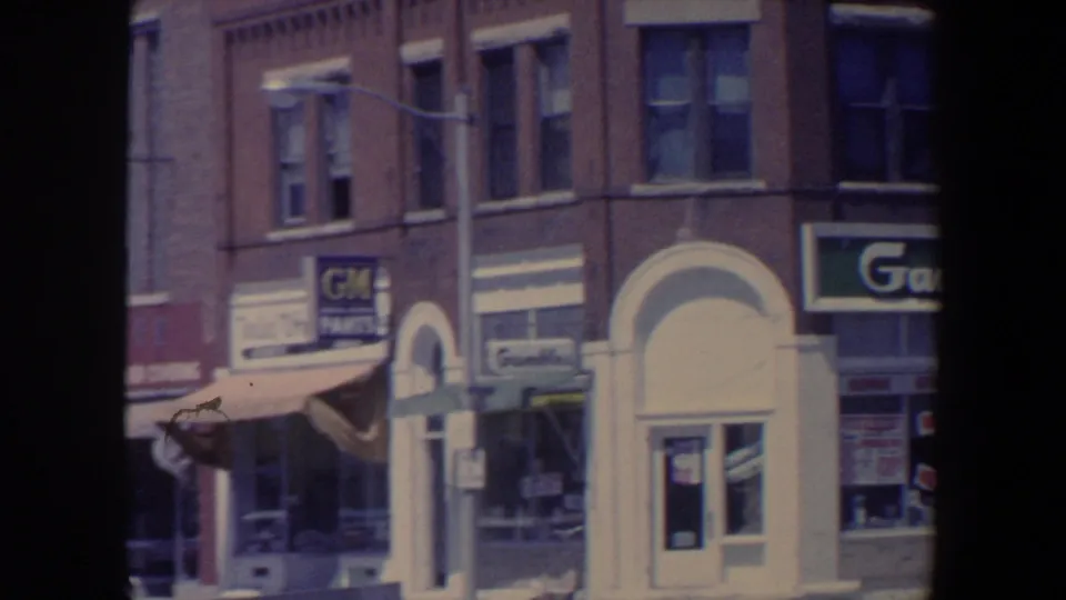 1959 Iowa commercial block showing awnings, an arched doorway, streetlight, and Gambles-style storefront signage.