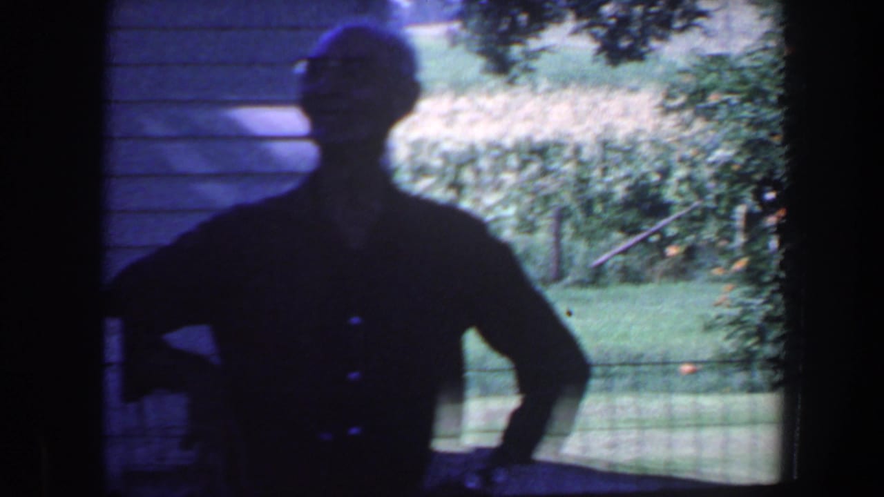 Senior man in silhouette stands near house siding with a bright yard and field behind him.