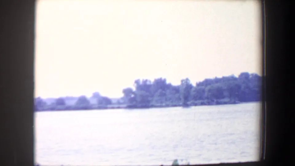 1959 Iowa 8mm frame showing open water and a distant wooded shoreline beneath a bright, washed-out sky.