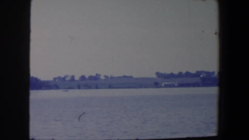 1959 Iowa 8mm frame showing open water, a far tree-lined shore, low hills, and faint shoreline structures.