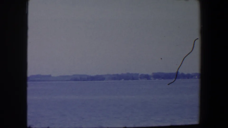 1959 Iowa shoreline view over calm water, with trees on the horizon and visible film handling marks.