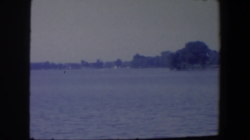 1959 Iowa water view with a wooded point or shoreline mass visible at right under an overcast sky.