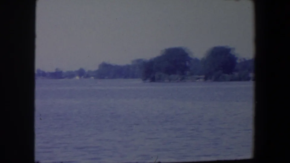 1959 Iowa 8mm frame showing calm lake water and a distant tree-lined shoreline in soft blue-toned color.