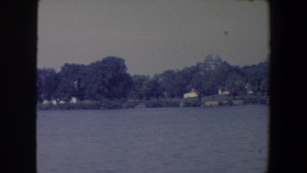 Calm lake with a tree-lined far shore and small distant structures.