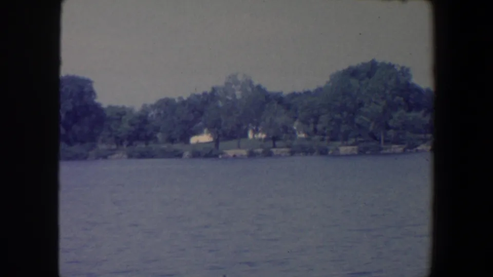 1959 Iowa lake view with rippled water, a wooded shoreline, and pale distant structures.