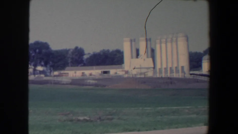 1959 Iowa farmstead view with multiple white silos, low structures, trees, and open field.