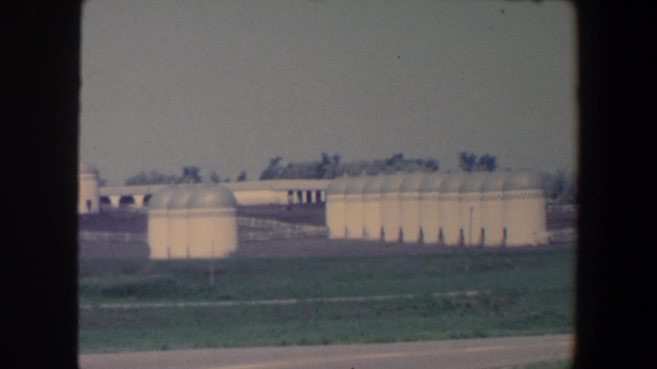 White silos and domed farm structures beyond grass and a road edge.