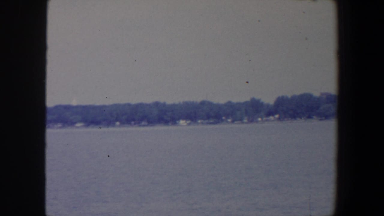Calm lake water with a distant tree-lined shore under a pale sky.