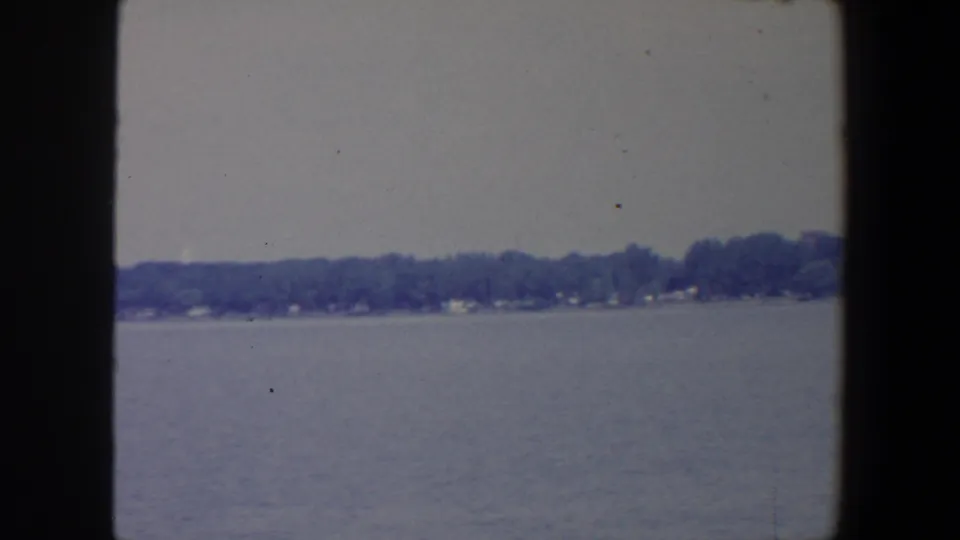1959 Iowa 8mm frame showing open lake water and a distant tree-lined shore from a boat viewpoint.
