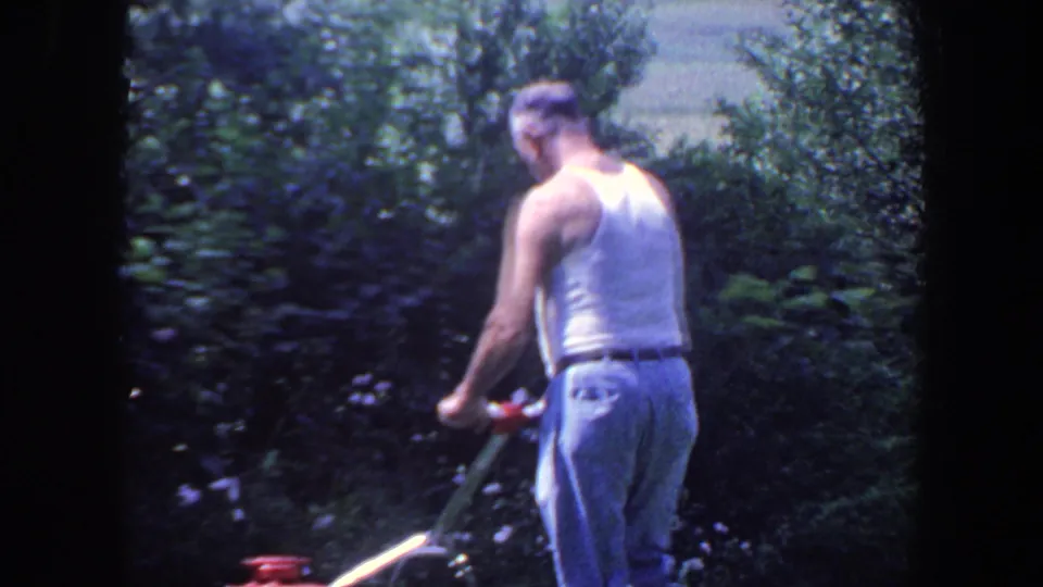 The man continues mowing in a leafy Iowa yard, framed from behind in soft 8mm color footage.