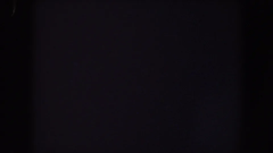 Near-total darkness in a 1959 Iowa 8mm home-movie frame, with faint grain and a small bluish light trace near the bottom.