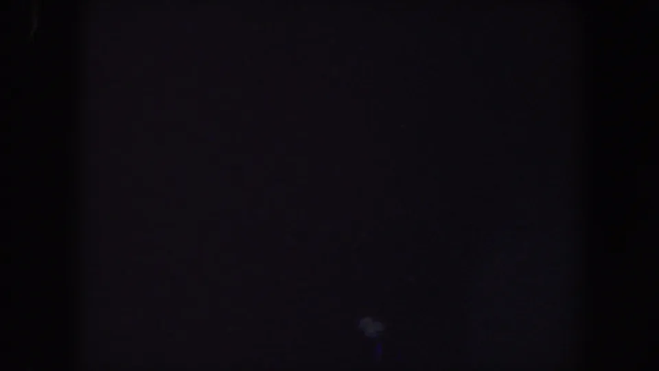 Dark 1959 Iowa home-movie frame with a central shadow band, muted grain, and a faint blue-purple haze low in the image.