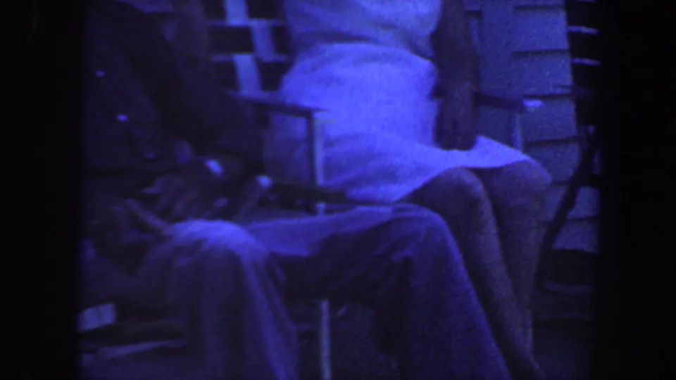 1959 Iowa porch footage with a small white dog filling much of the frame near a seated person and folding chair.