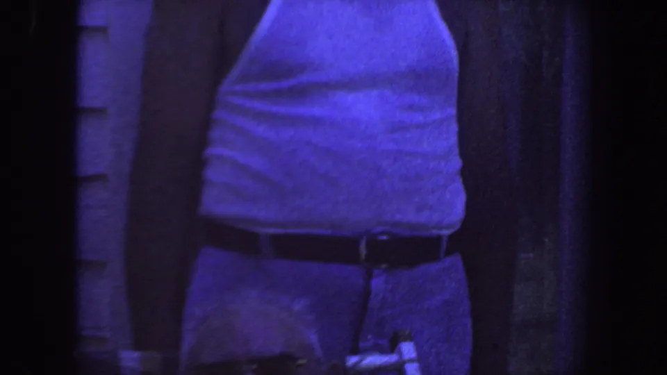 Cropped view of an adult man in a white tank top and belted trousers outdoors in 1959 Iowa home-movie footage.