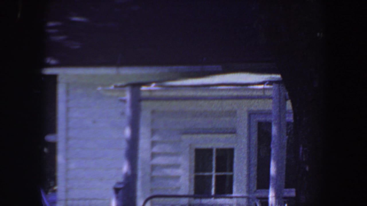 White clapboard house exterior with window and porch railing in shade.