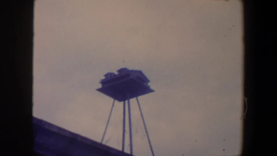 1959 Iowa home-movie frame showing the stilted structure from below, with a diagonal dark roof or foreground edge at lower left.