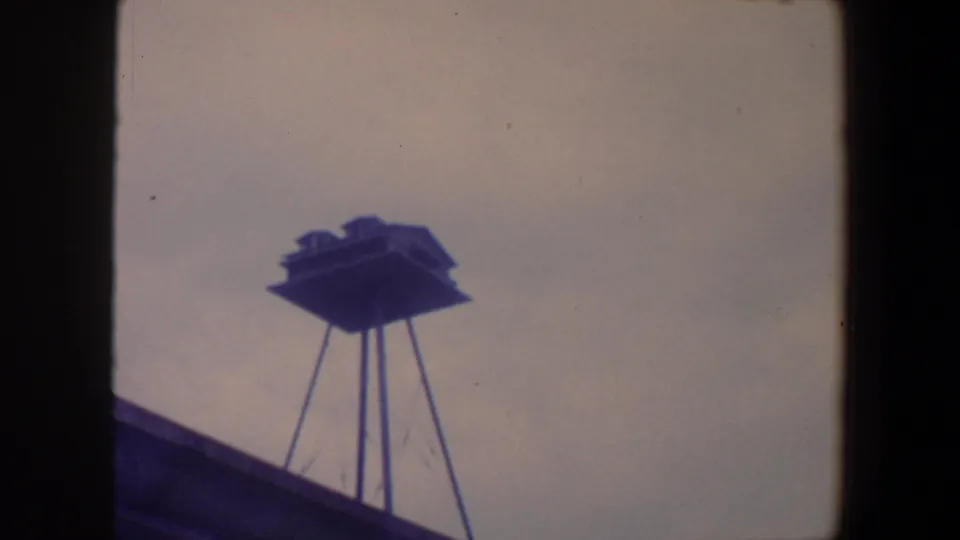 1959 Iowa 8mm frame showing the unidentified stilted structure centered against a pale sky with visible film wear.