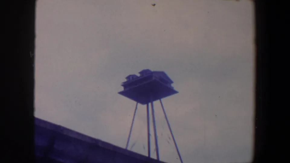 1959 Iowa 8mm still showing a small birdhouse structure silhouetted over a roofline with visible grain and dust.