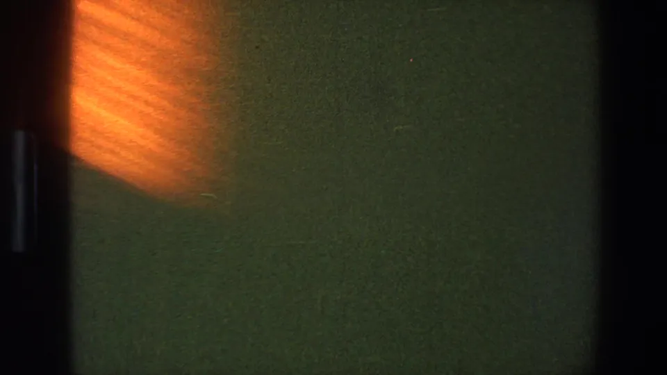 1973 Saint Paul 8mm frame with a mostly blank green field, black gate bar, grain, and a soft orange exposure flare.