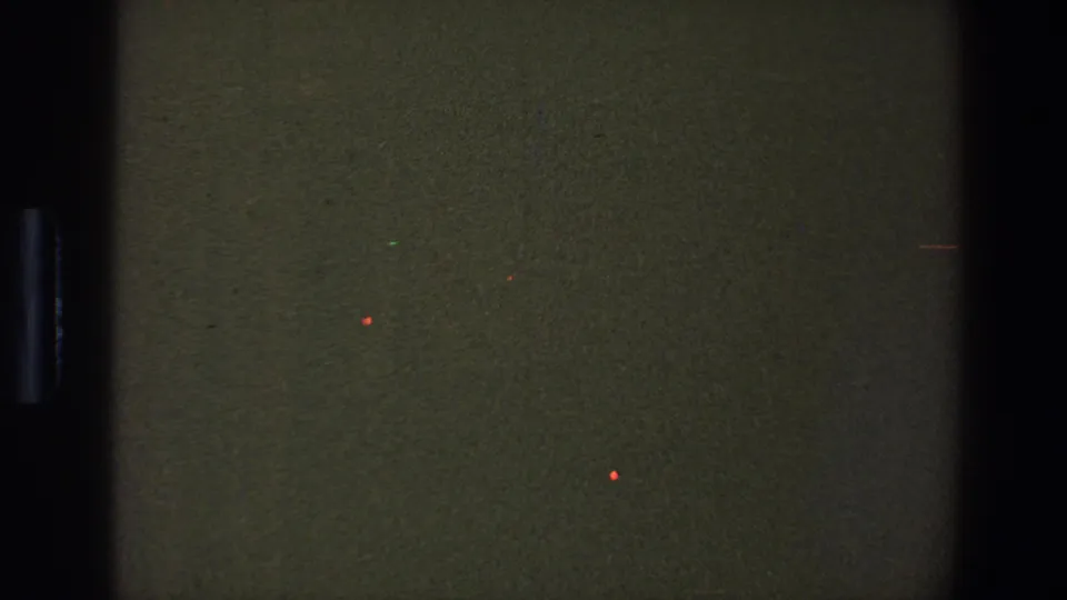 1973 Saint Paul 8mm frame showing a dim green-brown blank film area, black vertical strip, grain, and scattered red specks.