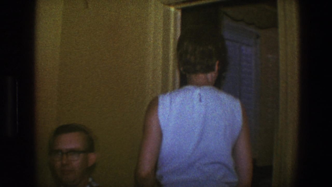 1973 Saint Paul home-movie frame showing adults in a private interior while a woman walks through a doorway.