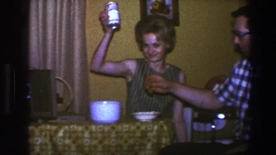 1973 Saint Paul home gathering with a woman raising a can near bowls and a man reaching across the table.