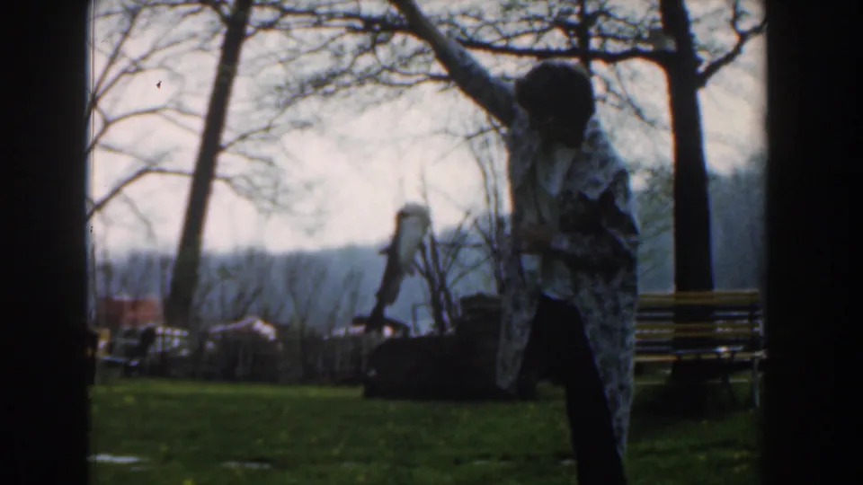 A woman in a patterned coat raises a small shark or fish on a pole in the Novi, Michigan park scene.