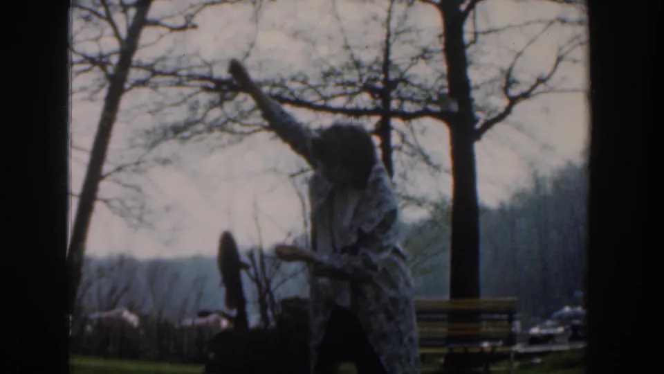 At the end of the clip, the woman lowers the pole with the small catch near a yellow bench and bare trees.
