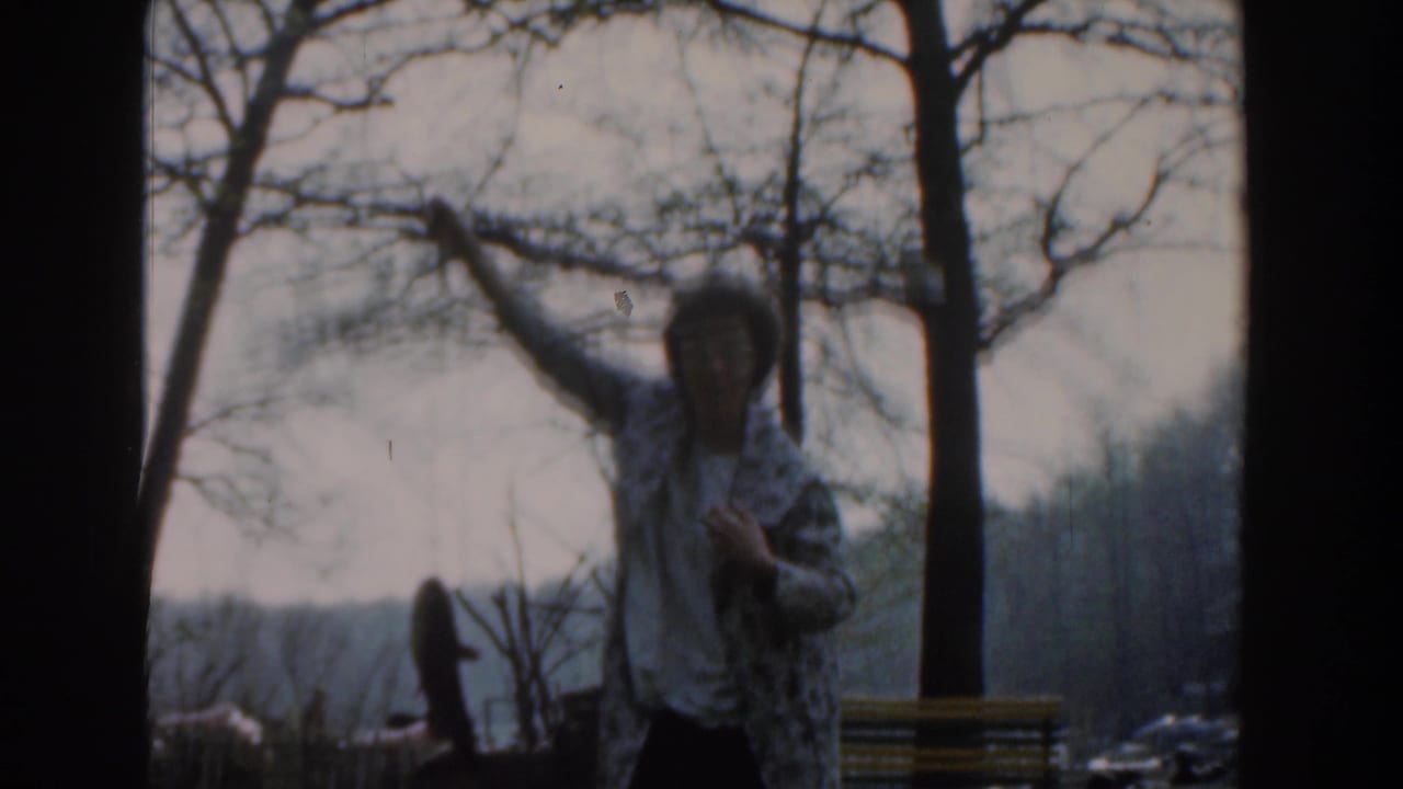 Woman faces the camera while raising a fish in a park with leafless trees.