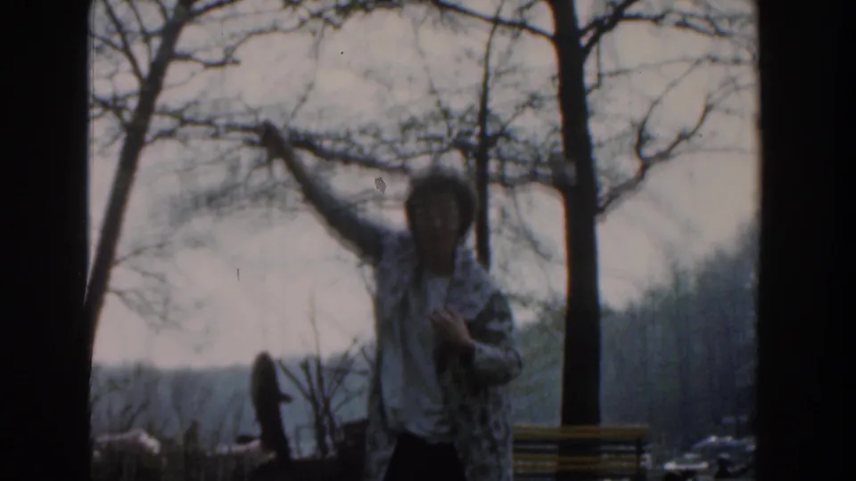 The woman faces the camera in a Novi park, holding a fish aloft against leafless trees and a muted sky.