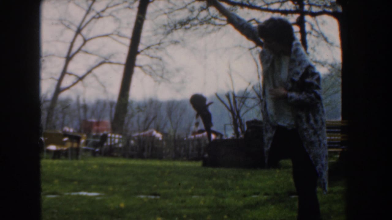 Person wrapped in a patterned blanket raises a fish on a grassy lawn near trees.