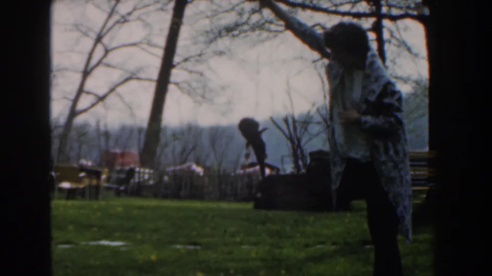 In 1961 Novi, Michigan footage, a blanket-wrapped person stands outdoors with one arm raised holding a fish.