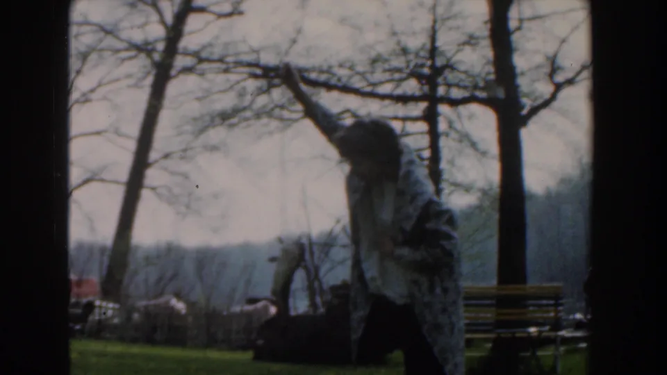 A closer 1961 home-movie frame shows the person wrapped in a gray-white blanket holding a fish outdoors.