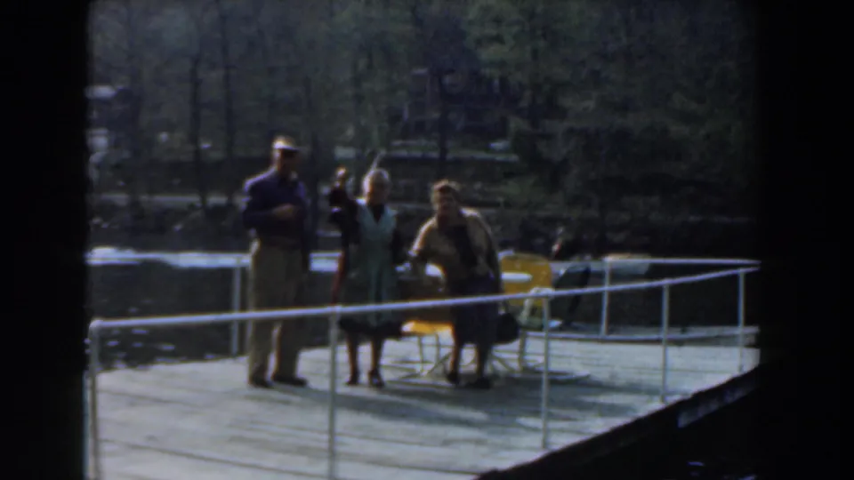 Three adults stand together on a dock in Novi, Michigan, 1961, with railings, water, and fishing gear visible.
