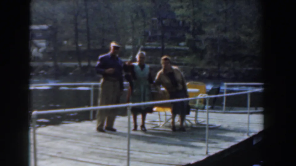 The group remains on the Novi lakeside dock, with yellow folding chairs, white railings, water, and trees visible in the background.