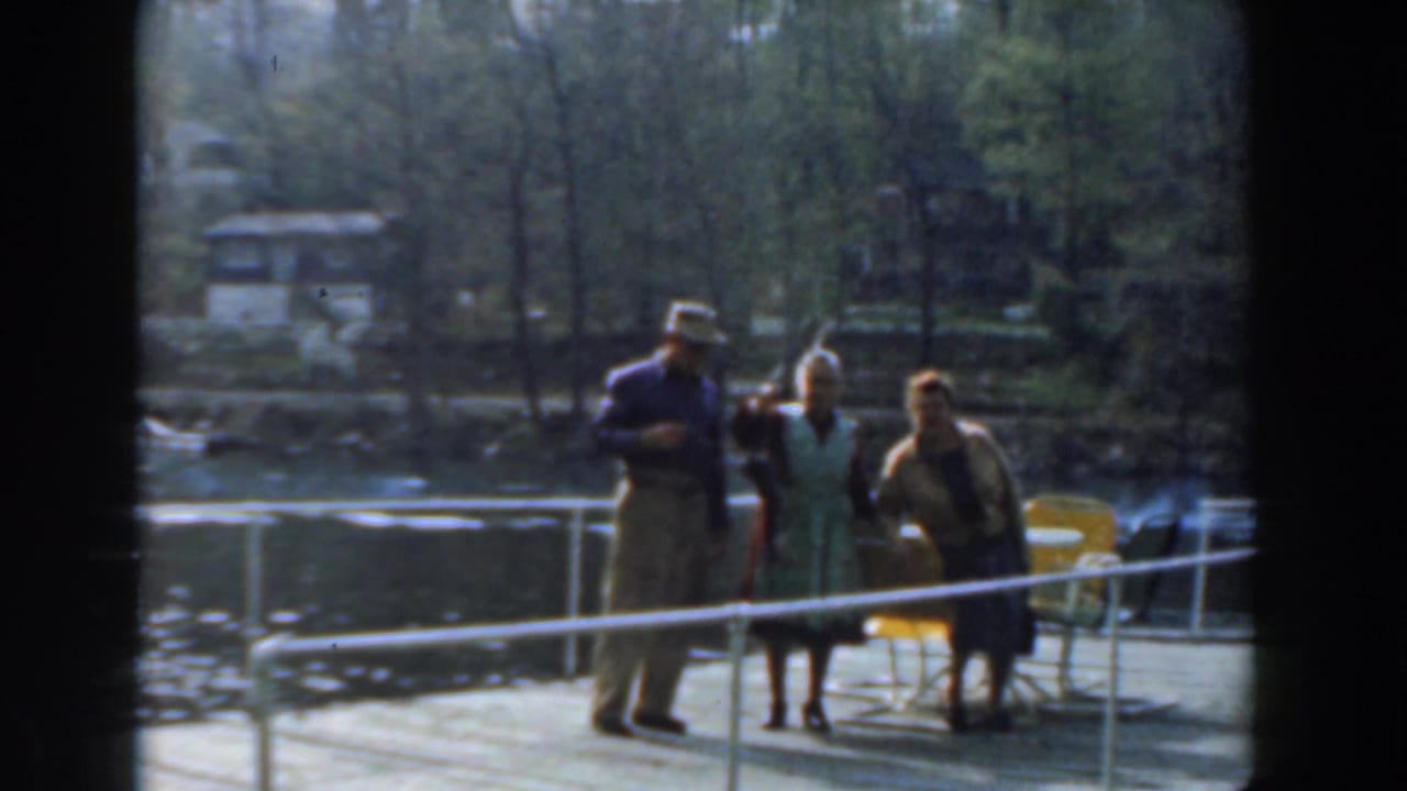 Three adults stand on a wooden pier by water, with one holding up a fish.