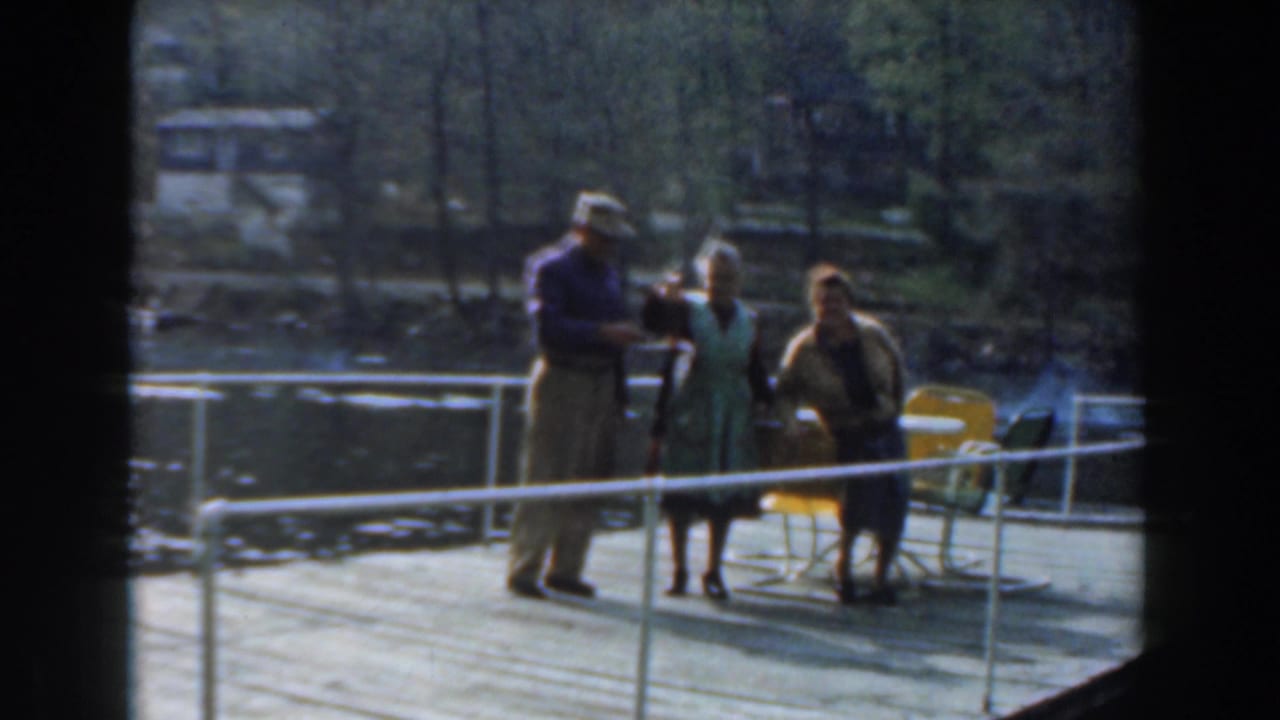 Three adults on a pier face the camera near chairs and a white railing.