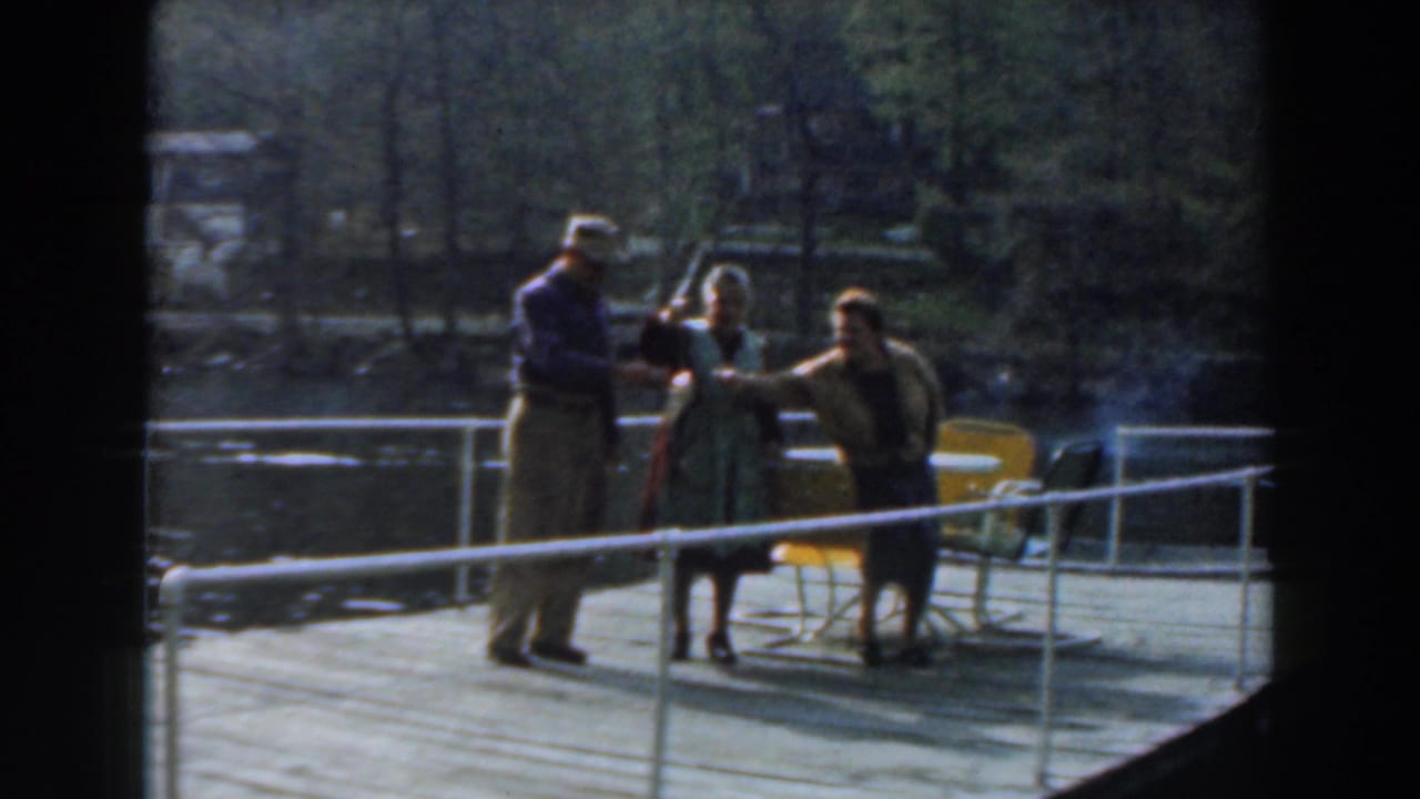 In Novi, Michigan in 1961, three adults stand on a dock by calm water as a fish is displayed toward the camera.
