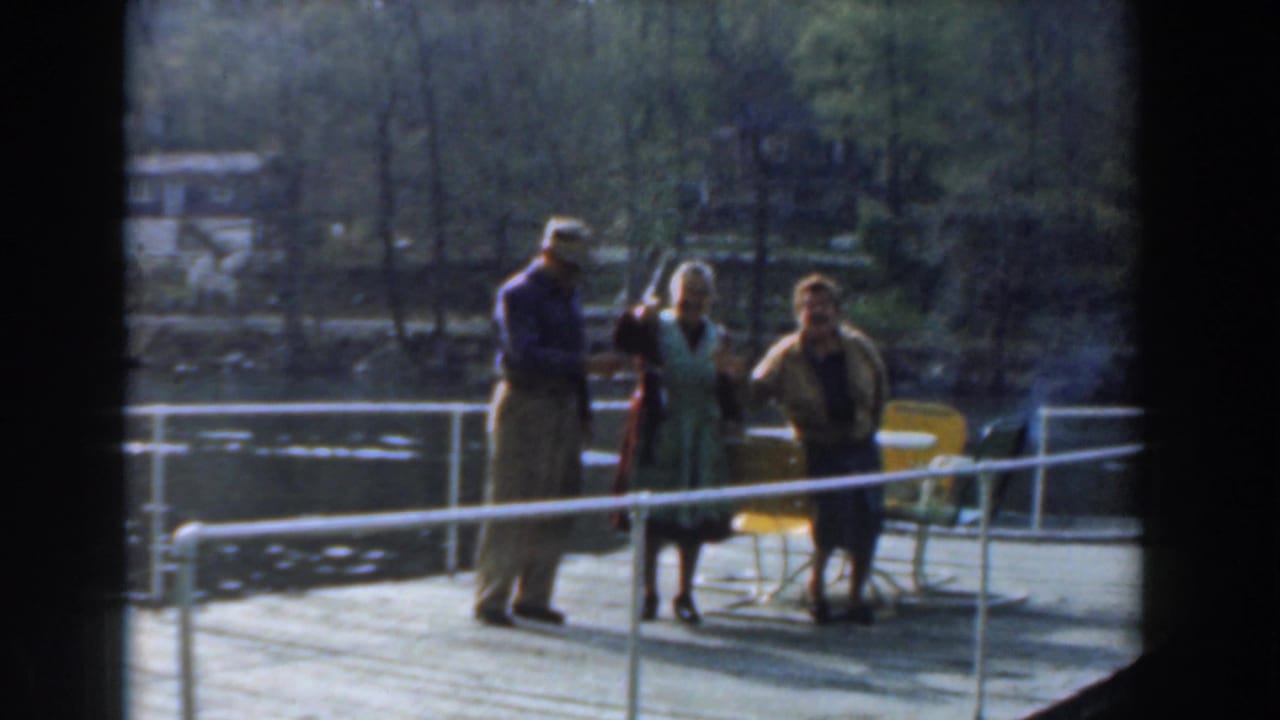 Three adults pose by a dock railing with a fish raised between them.