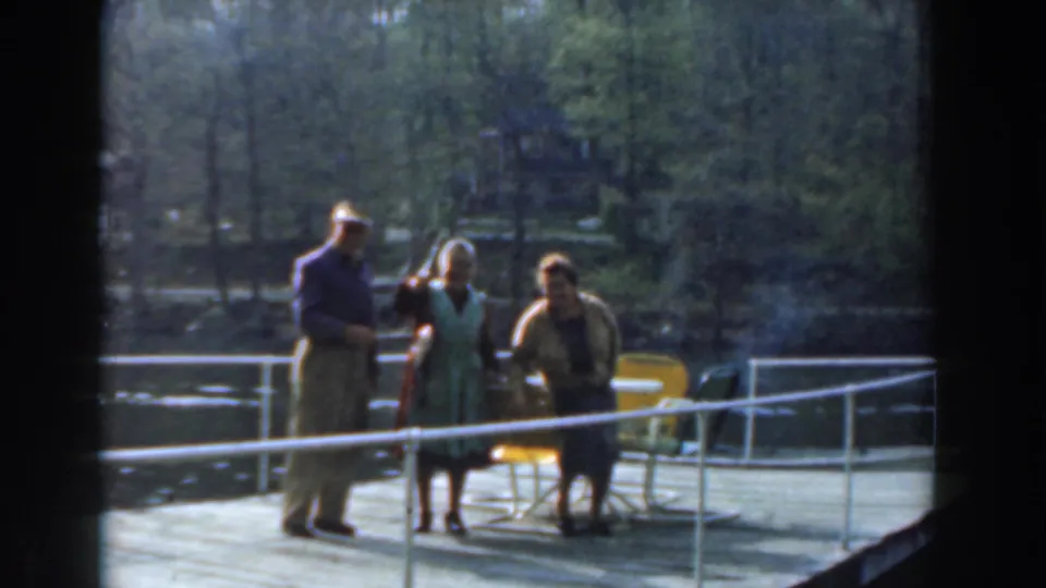 A man in a hat and two women stand on a lakeside dock in 1961 Novi, with the fish still being shown near the center.