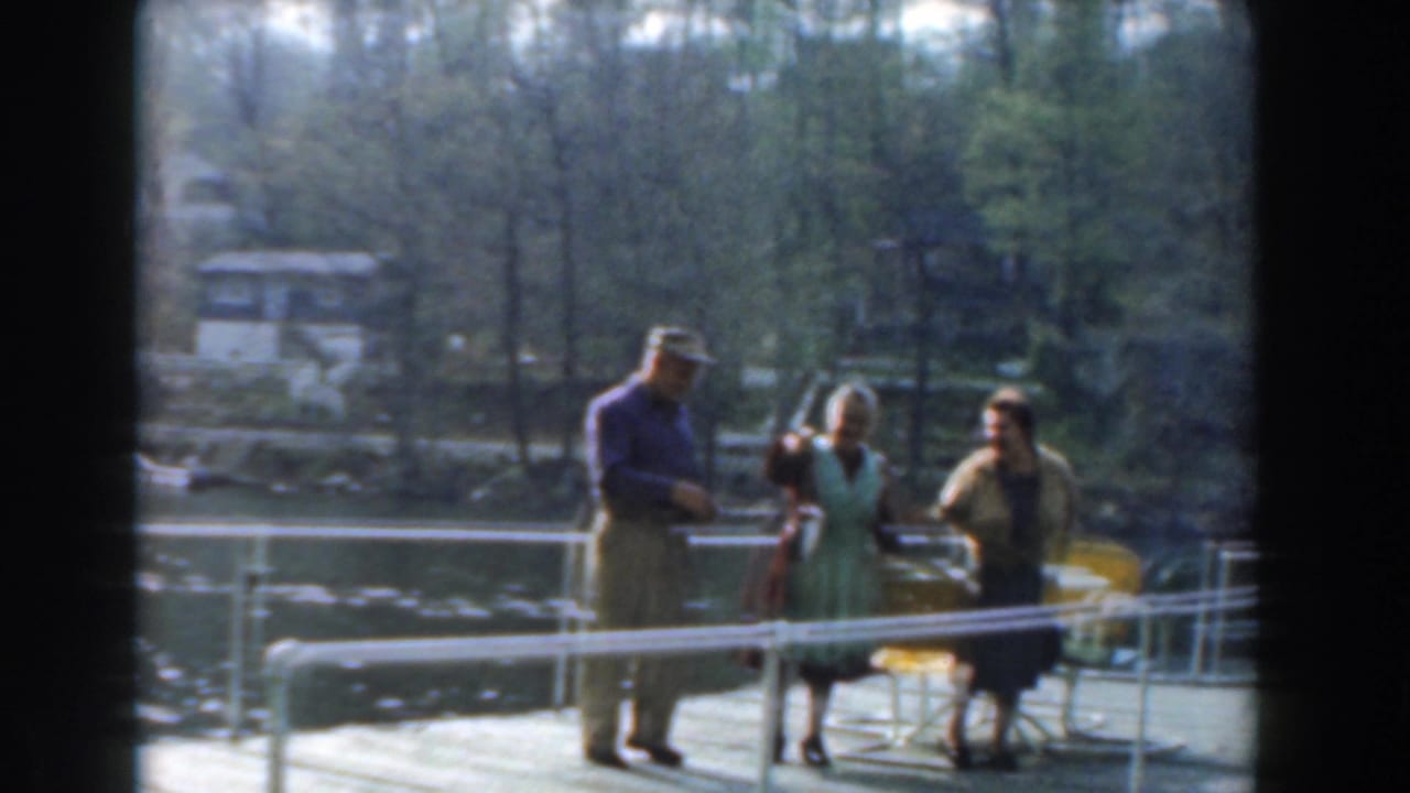 A man and two women stand near yellow chairs on a pier beside the water.
