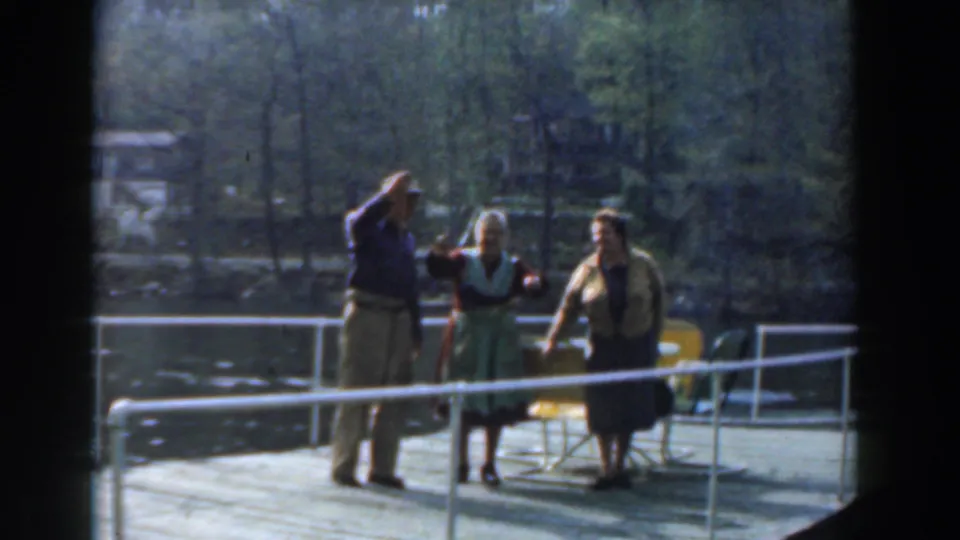 The man raises his hand again as the two women stand beside him on the Novi lakeside pier in soft 8mm footage.